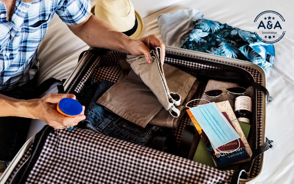una persona arreglando su maleta en la que hay pantalones, camisas,, tapabocas, gafas, preparándose para viajar